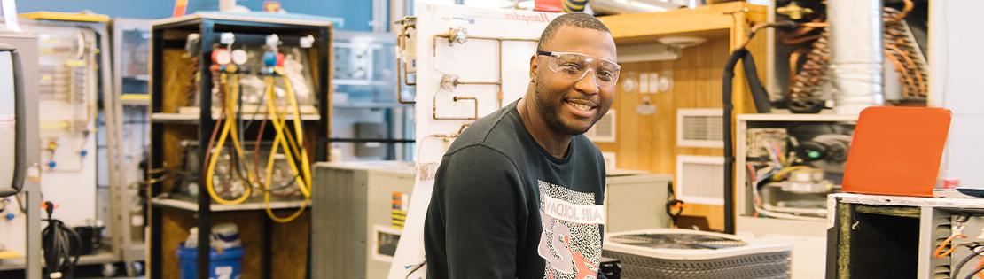 A student sits smiling with safety glasses in an engineering lab